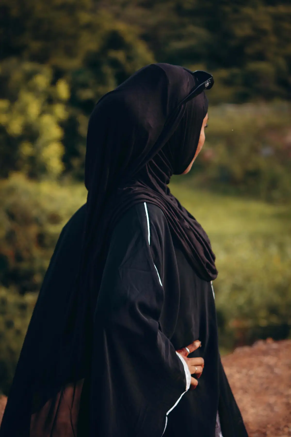 Side view of a woman in a black abaya and hijab in a green garden