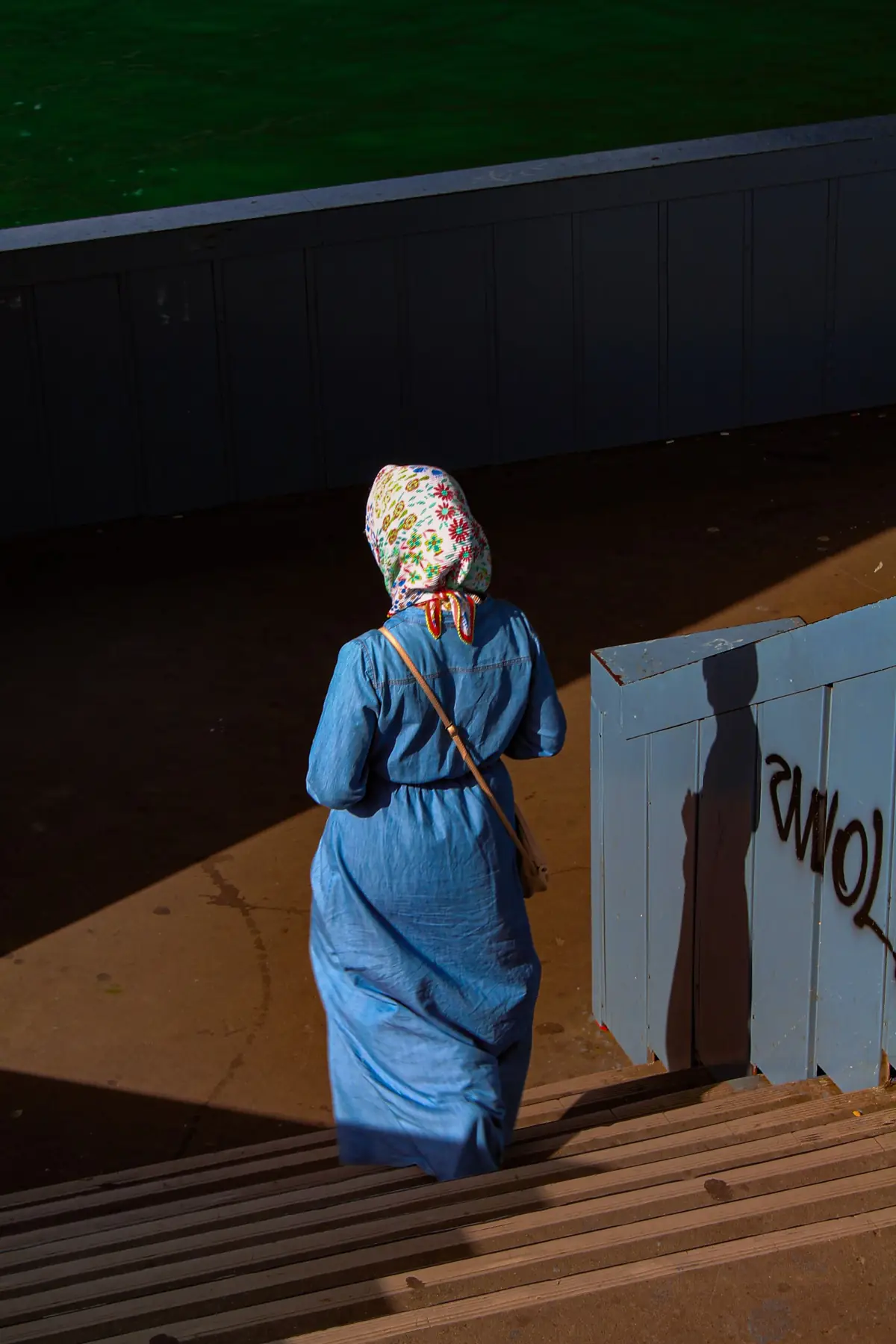A woman in a blue dress and printed hijab walking down sunlit stairs